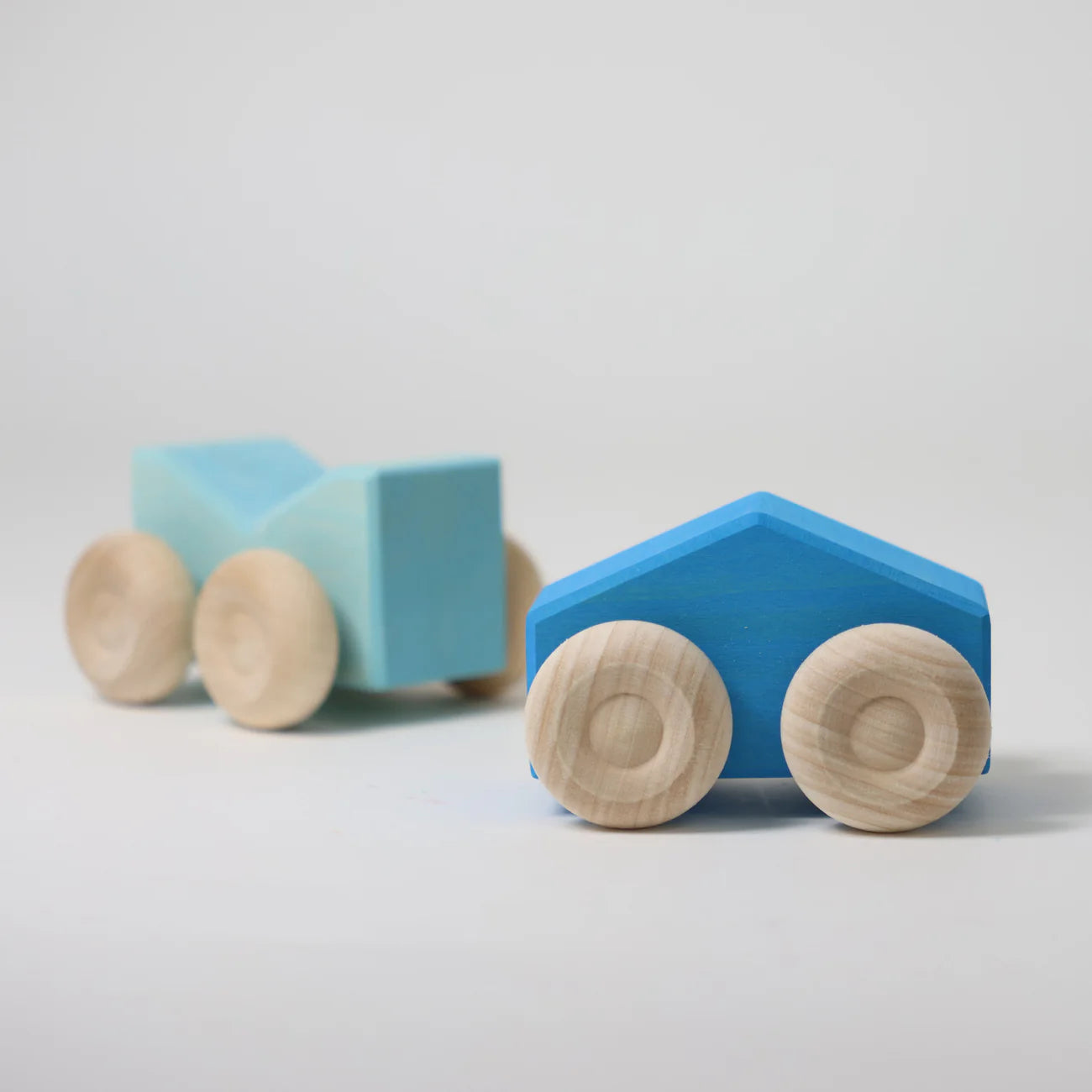 Two blue wooden toy cars with round wooden wheels on a light gray background