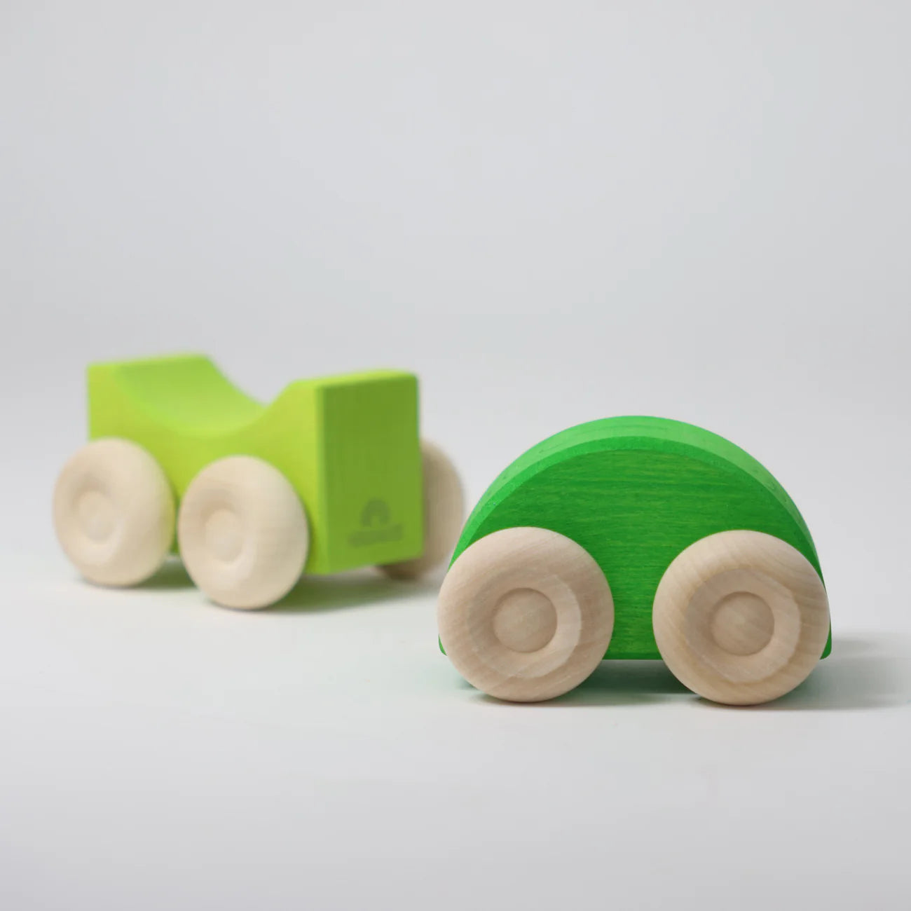 Two green wooden toy cars on a light gray background