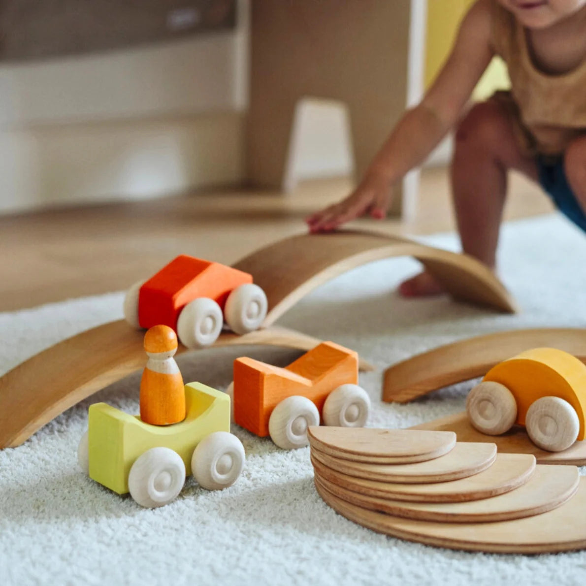 Wooden toy train set on a carpeted floor with a child in the background.