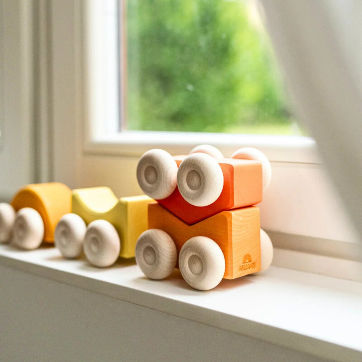 Colorful wooden toy train on a windowsill with a blurred green garden background