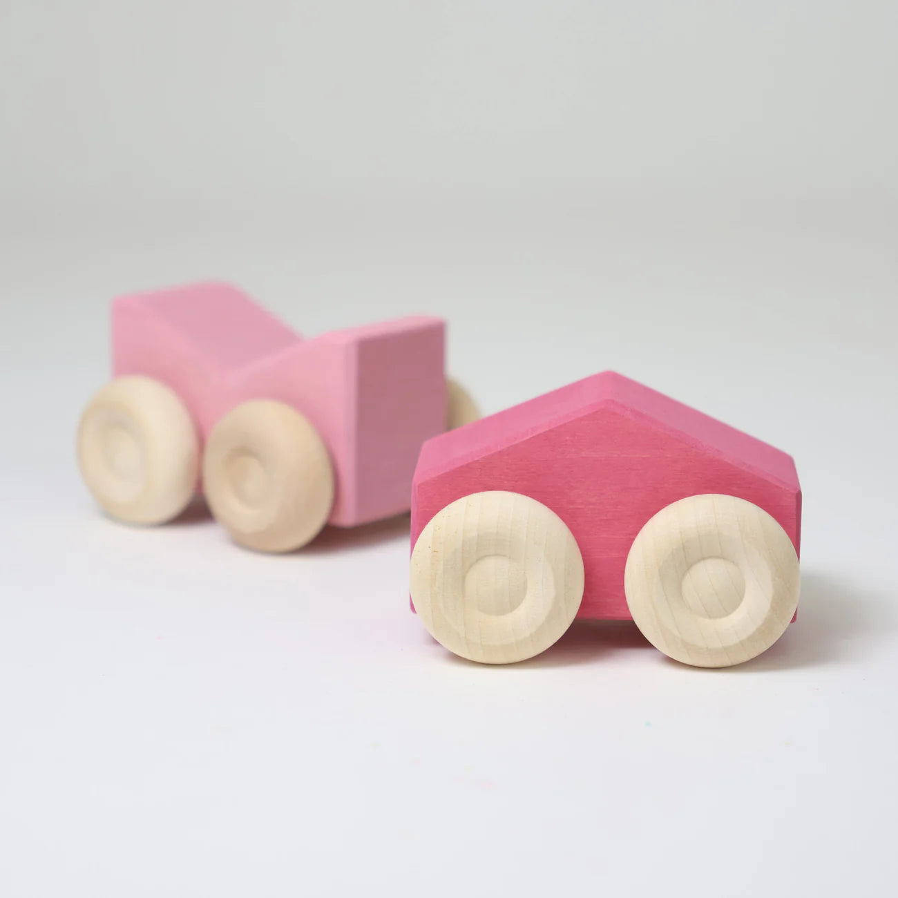 Two pink wooden toy cars with beige wheels on a light gray background