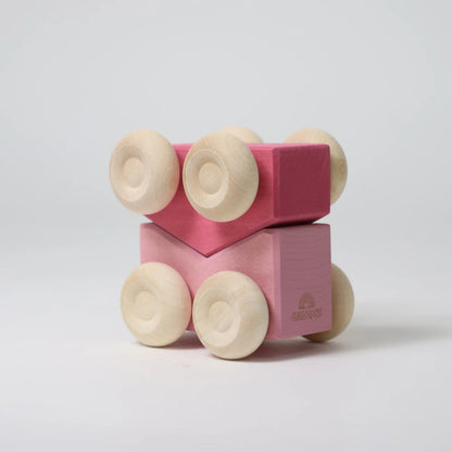 Pink wooden block with wheels on a light gray background
