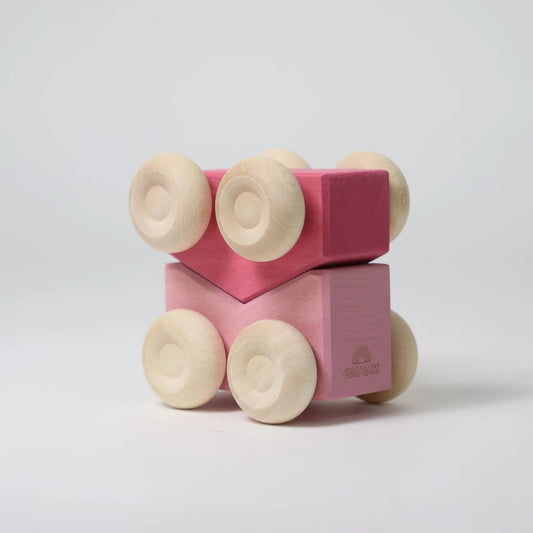 Pink wooden block with wheels on a light gray background