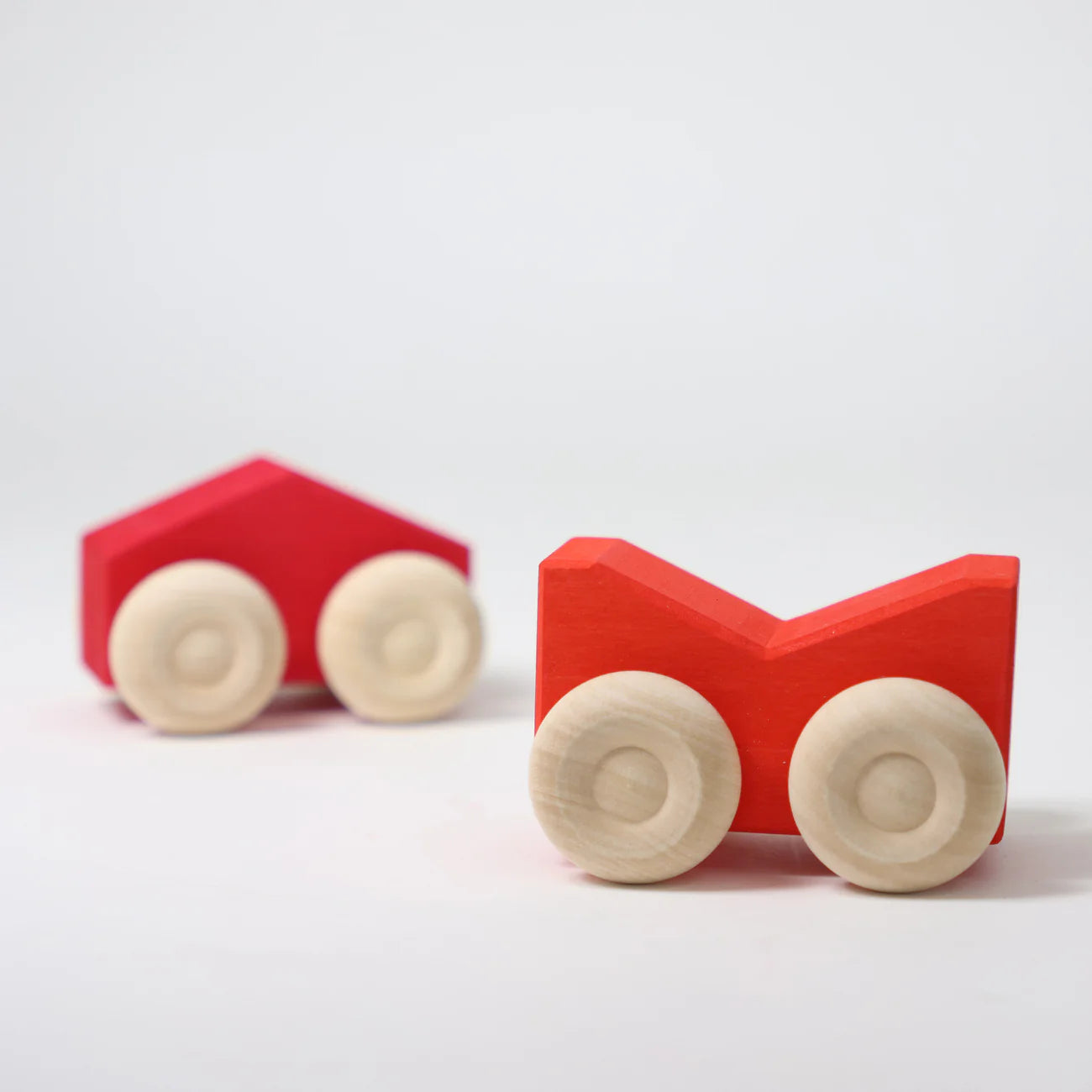 Two red wooden toys with beige wheels on a white background
