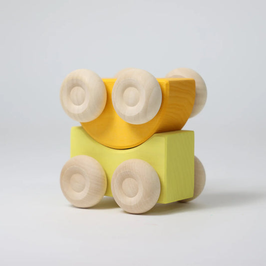 Wooden toy with yellow block and beige wheels on a light gray background