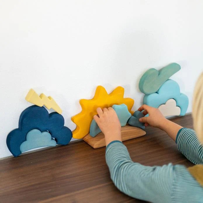 Children playing with colorful wooden shapes on a table against a white wall.