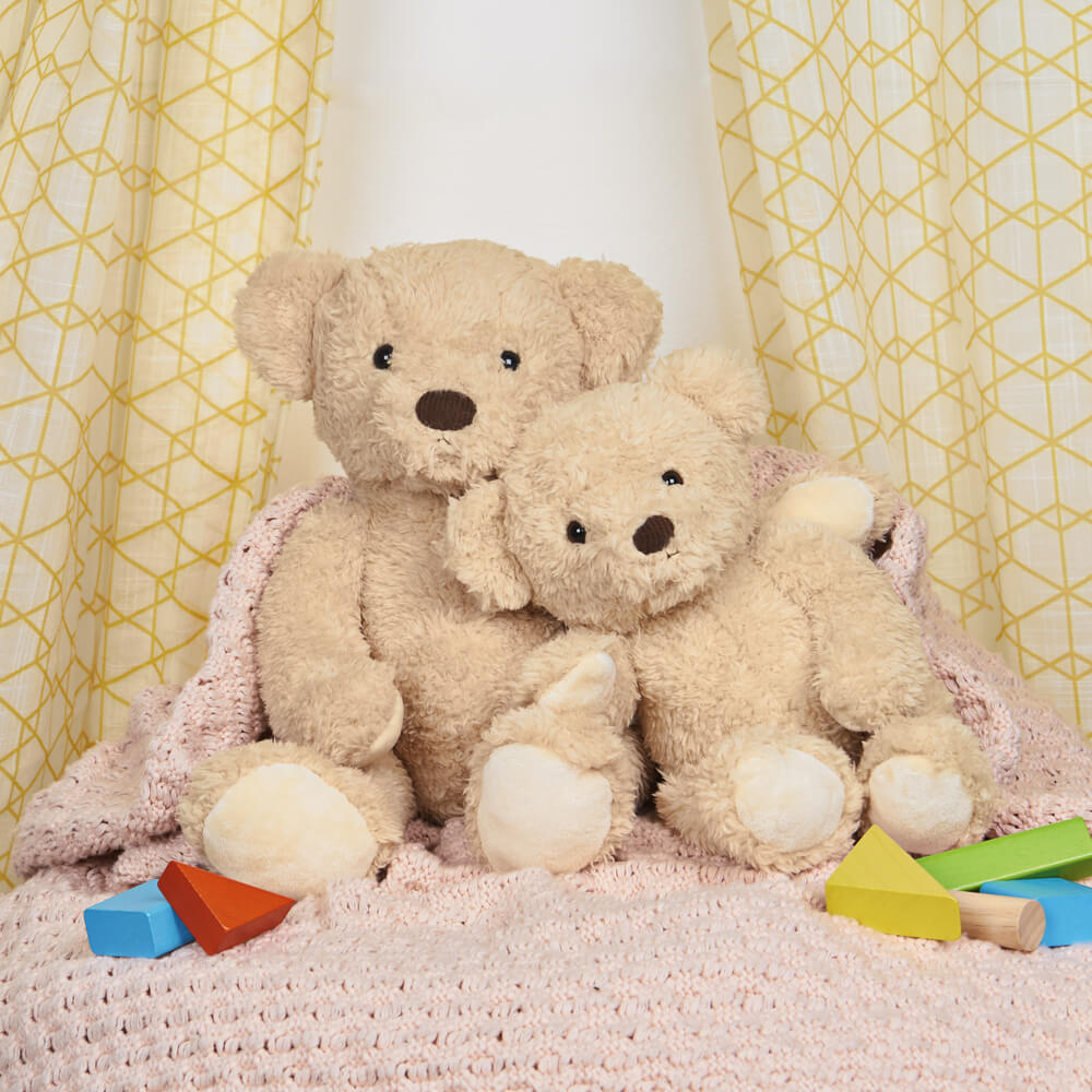 Two teddy bears sitting on a pink blanket with colorful blocks around them, against a yellow geometric-patterned curtain.