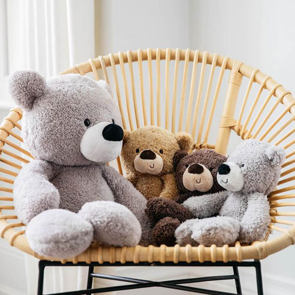 Four teddy bears of different colors sitting on a wicker chair.