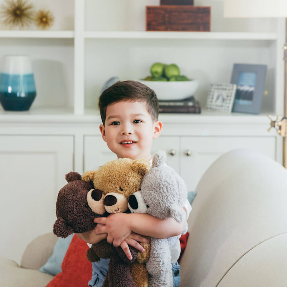 Child holding teddy bears in a living room setting