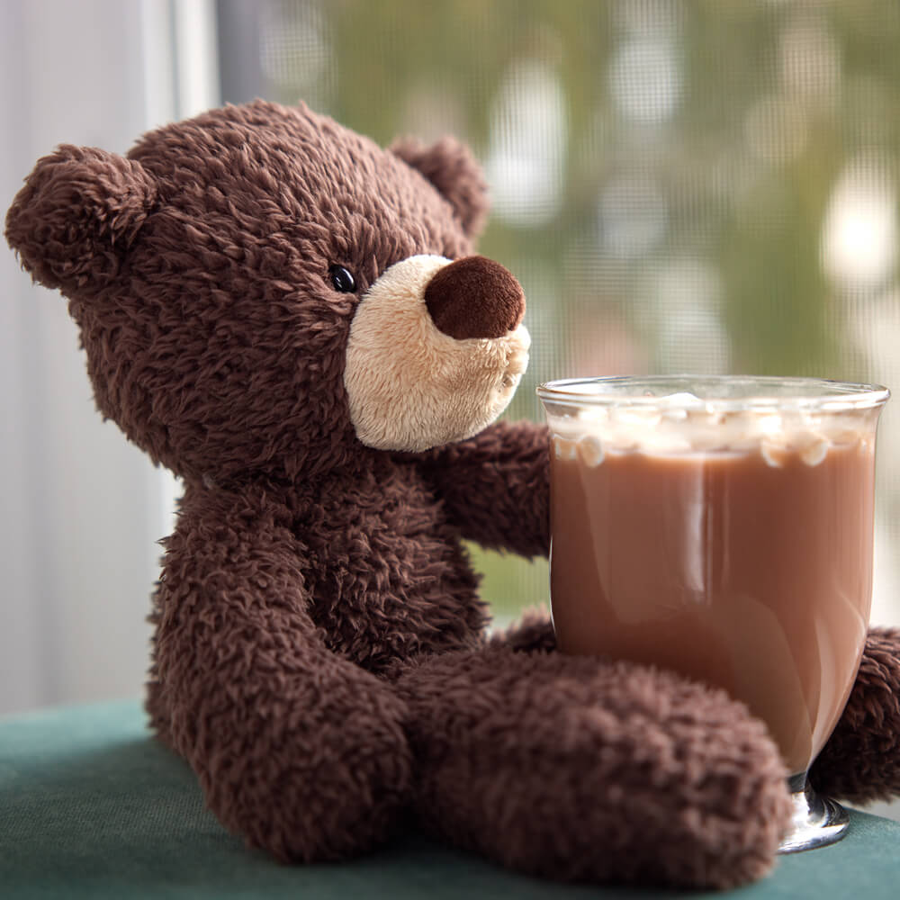 Brown teddy bear holding a glass of iced coffee on a green surface.