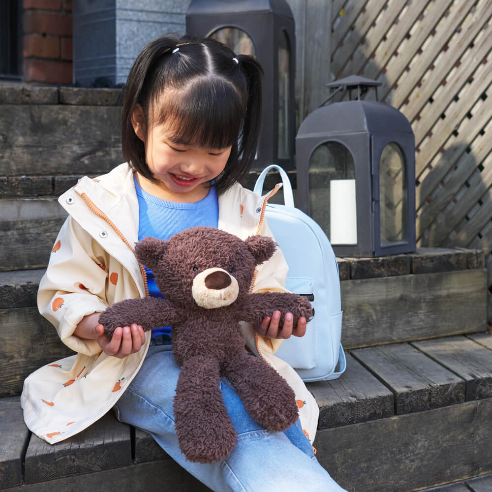 Child holding a teddy bear outdoors on wooden steps