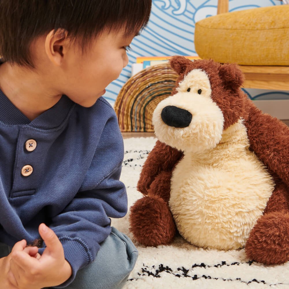 Child sitting next to a plush dog toy on a carpeted floor.