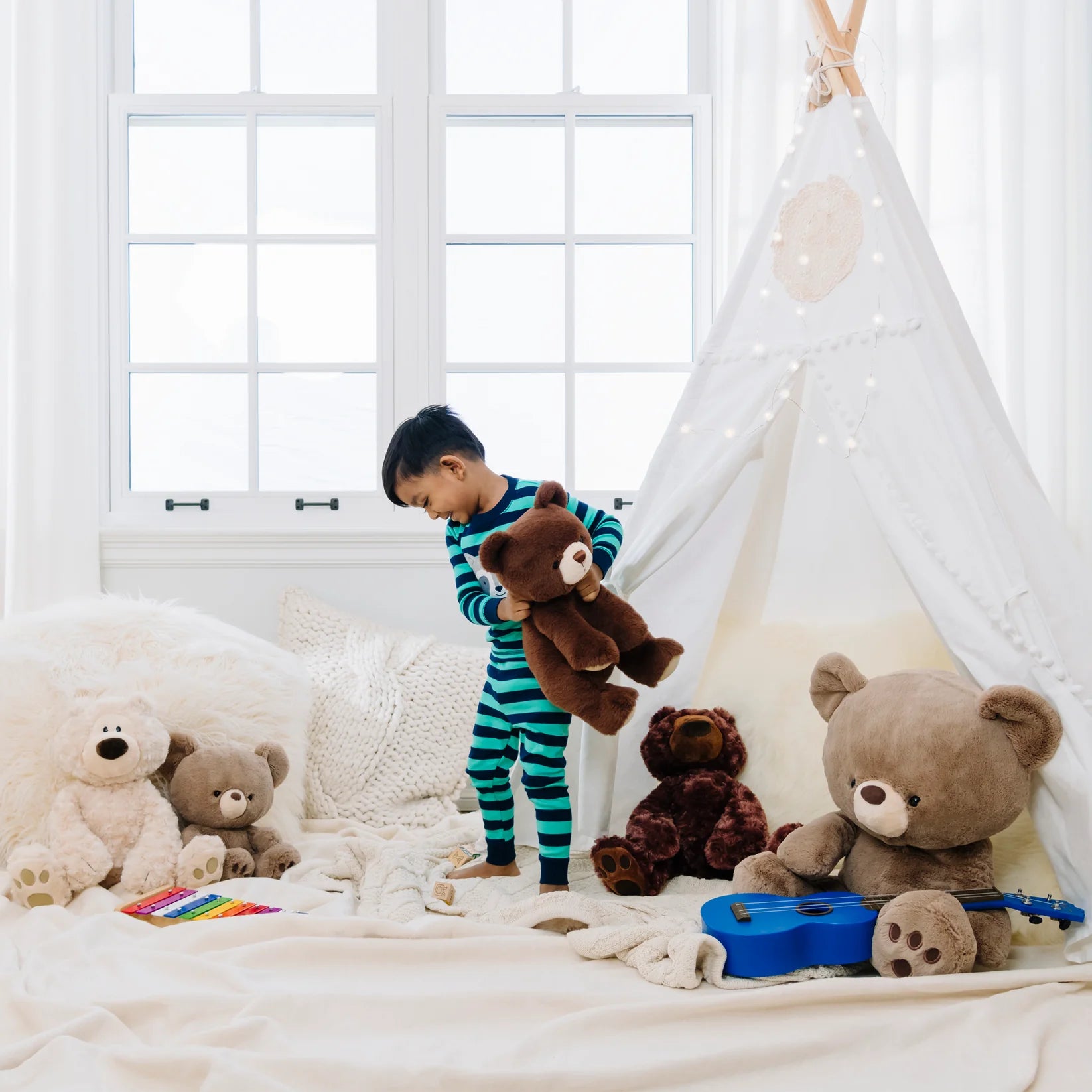 Child playing with teddy bears in a room with a white window and teepee.