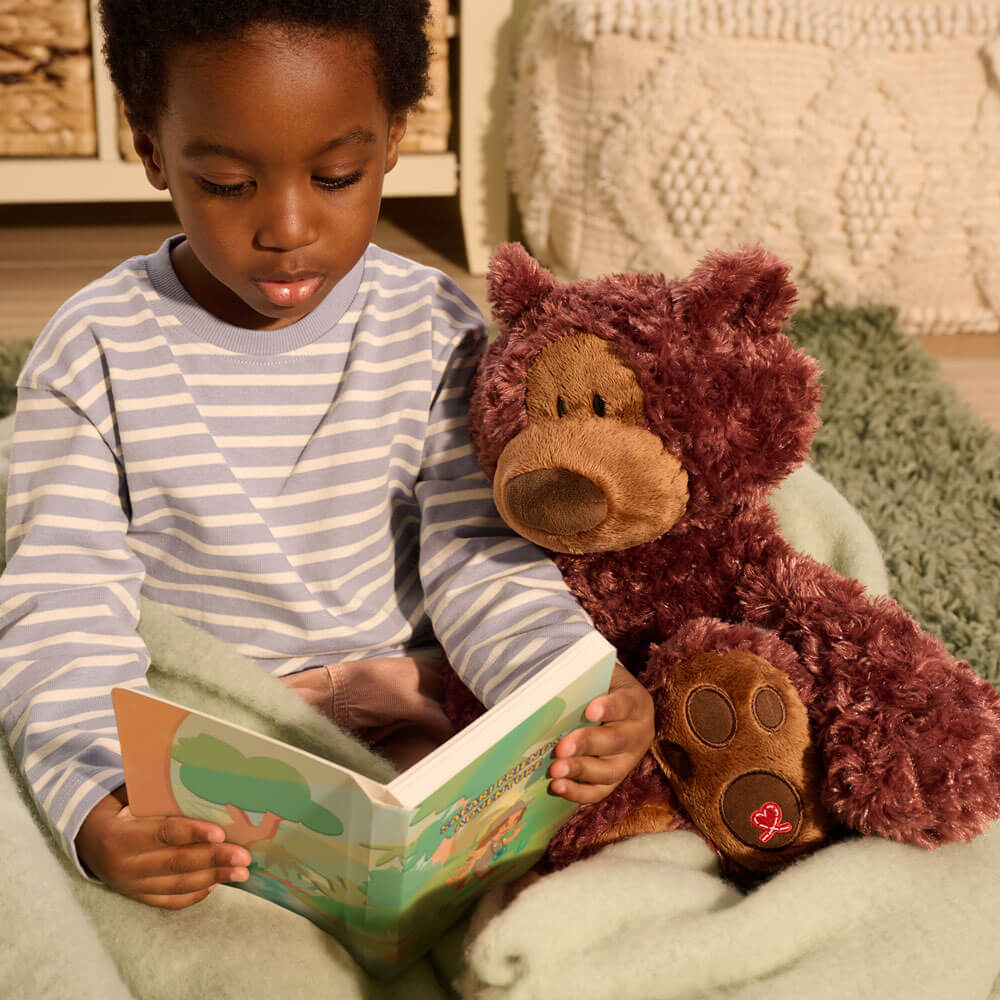Child reading a book to a teddy bear on a soft surface