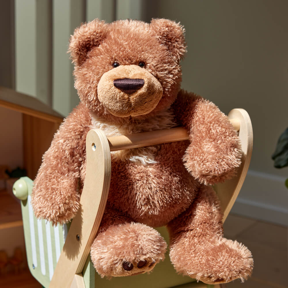 Brown teddy bear sitting on a wooden chair with a blurred background
