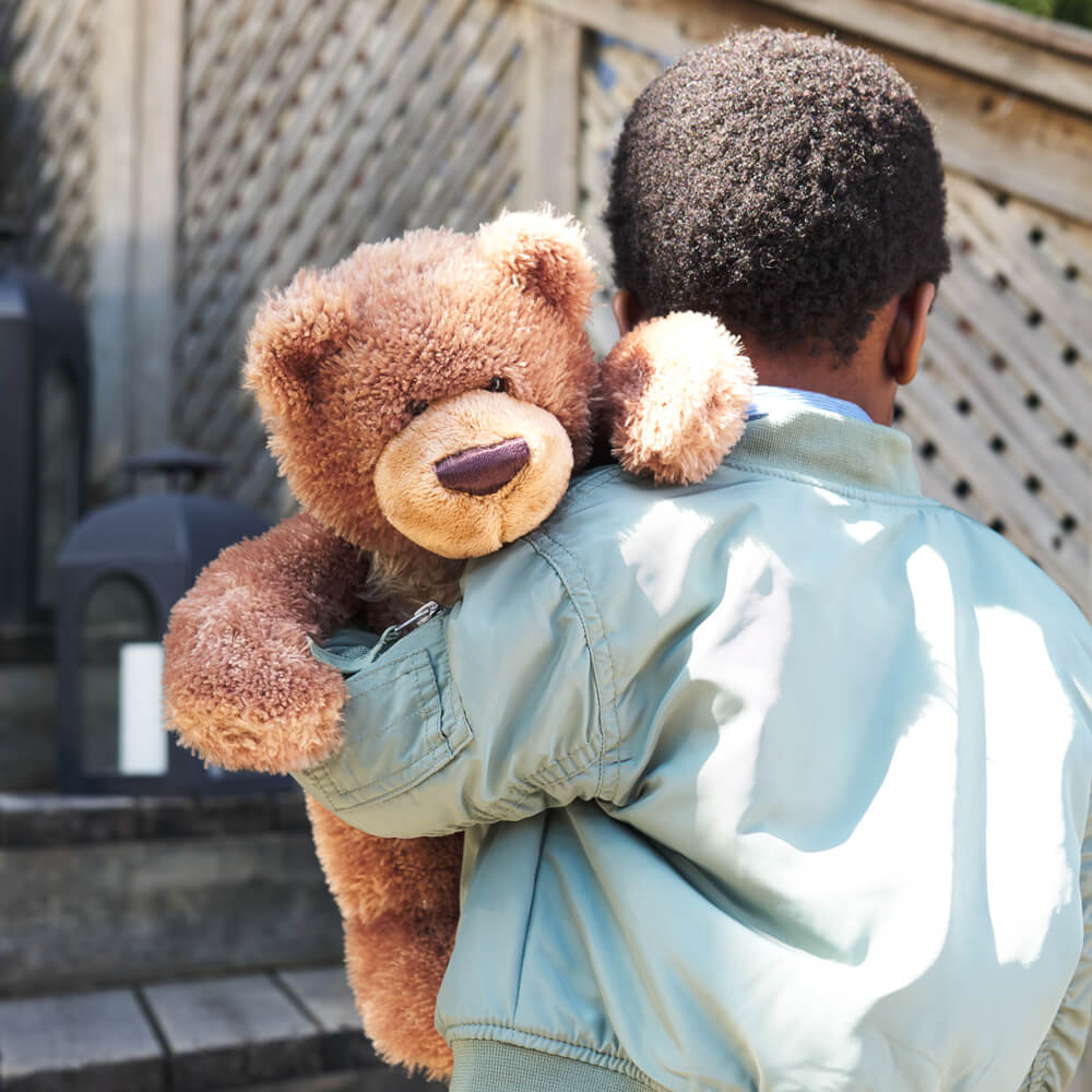 Person holding a large teddy bear outdoors on a wooden deck.