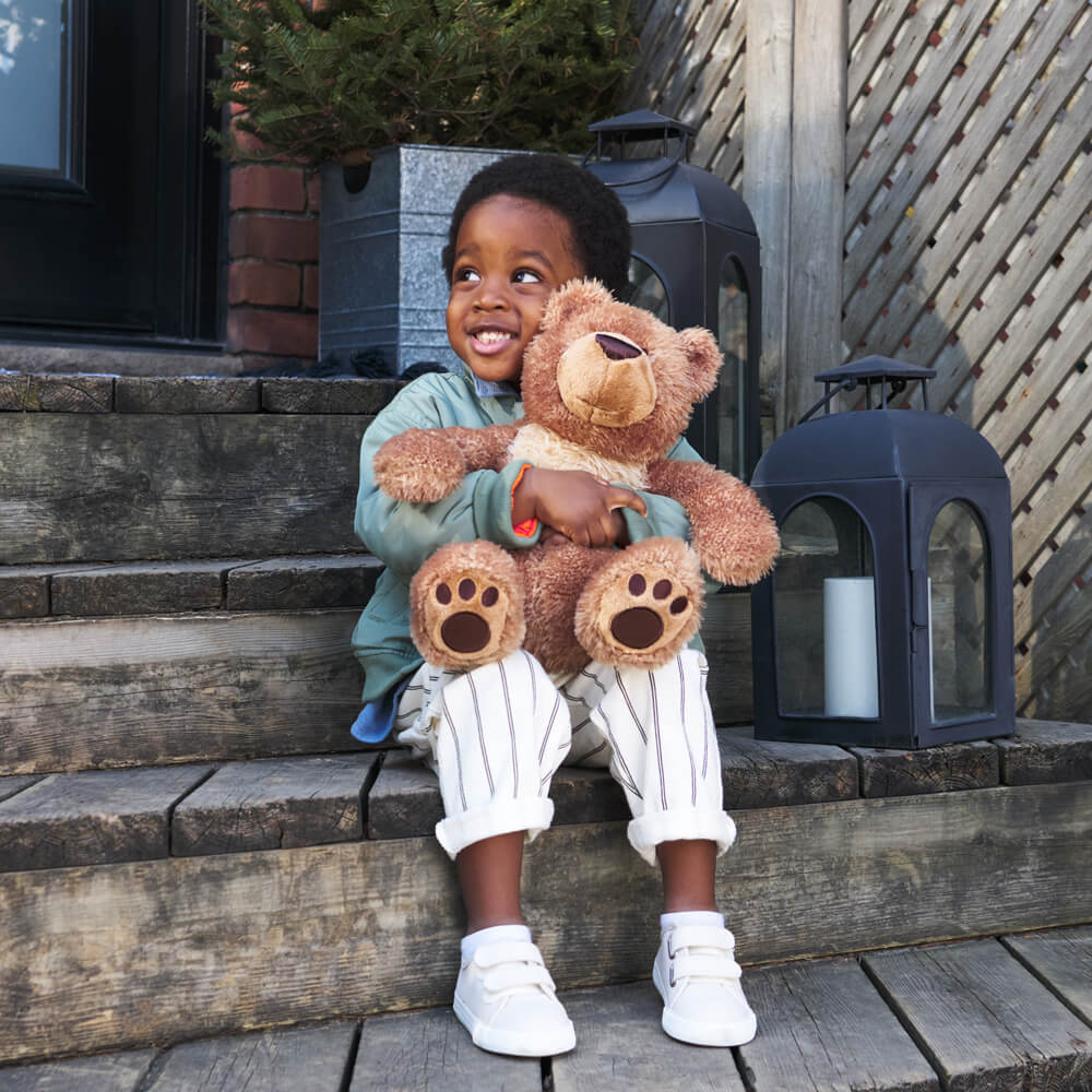 Child holding a teddy bear on outdoor steps with lanterns in the background