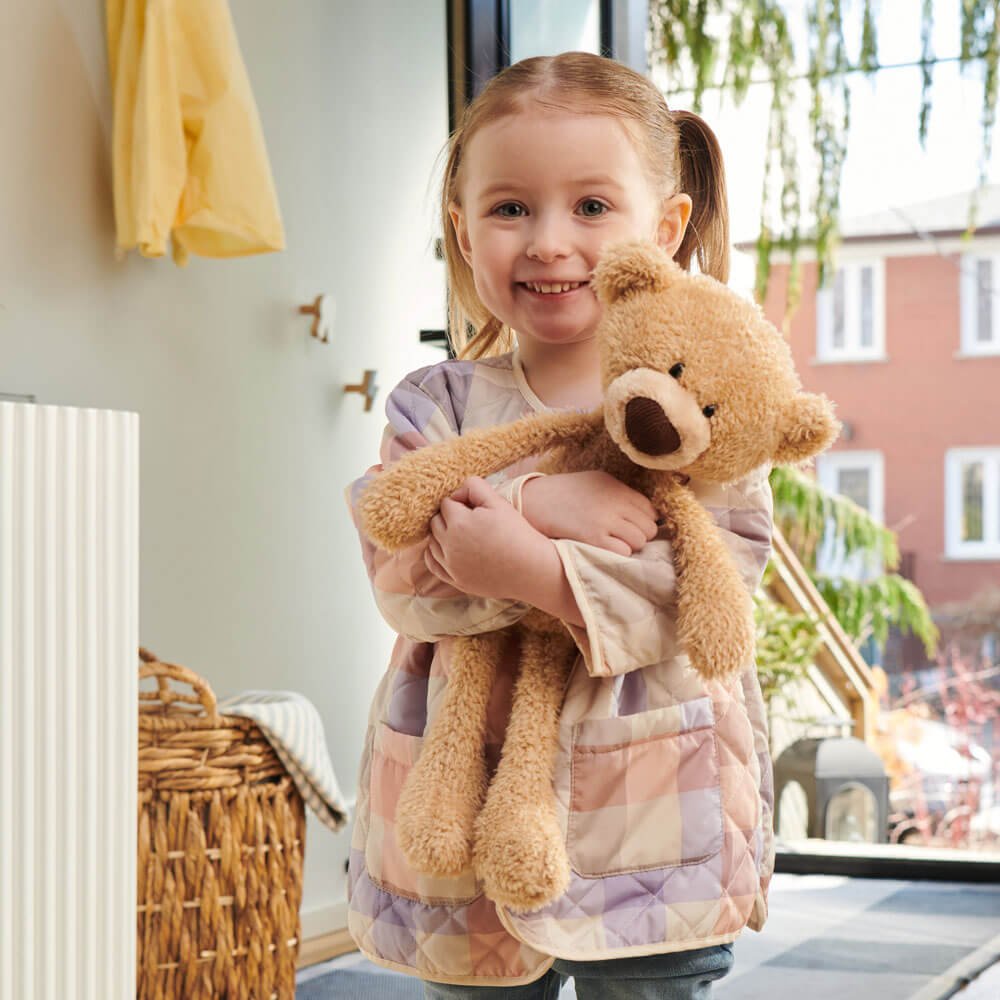 Child holding a teddy bear in a room with a window view