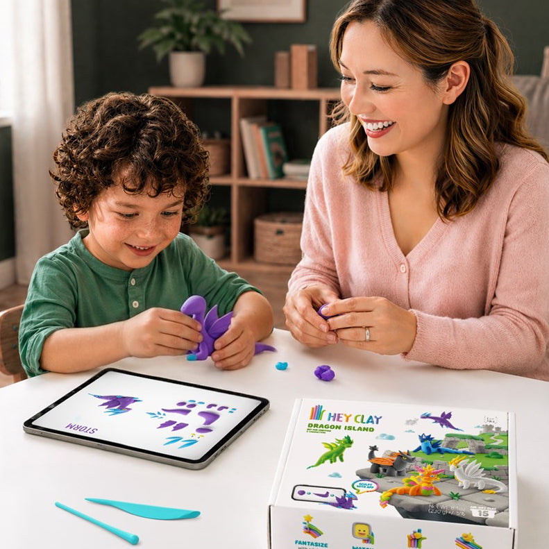 A woman and a young boy are sitting at a white table playing with a Dragon Clay set. The boy is molding a purple dinosaur with his hands while the woman smiles next to him.