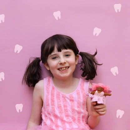 Young girl with pigtails holding a doll against a pink background with tooth illustrations