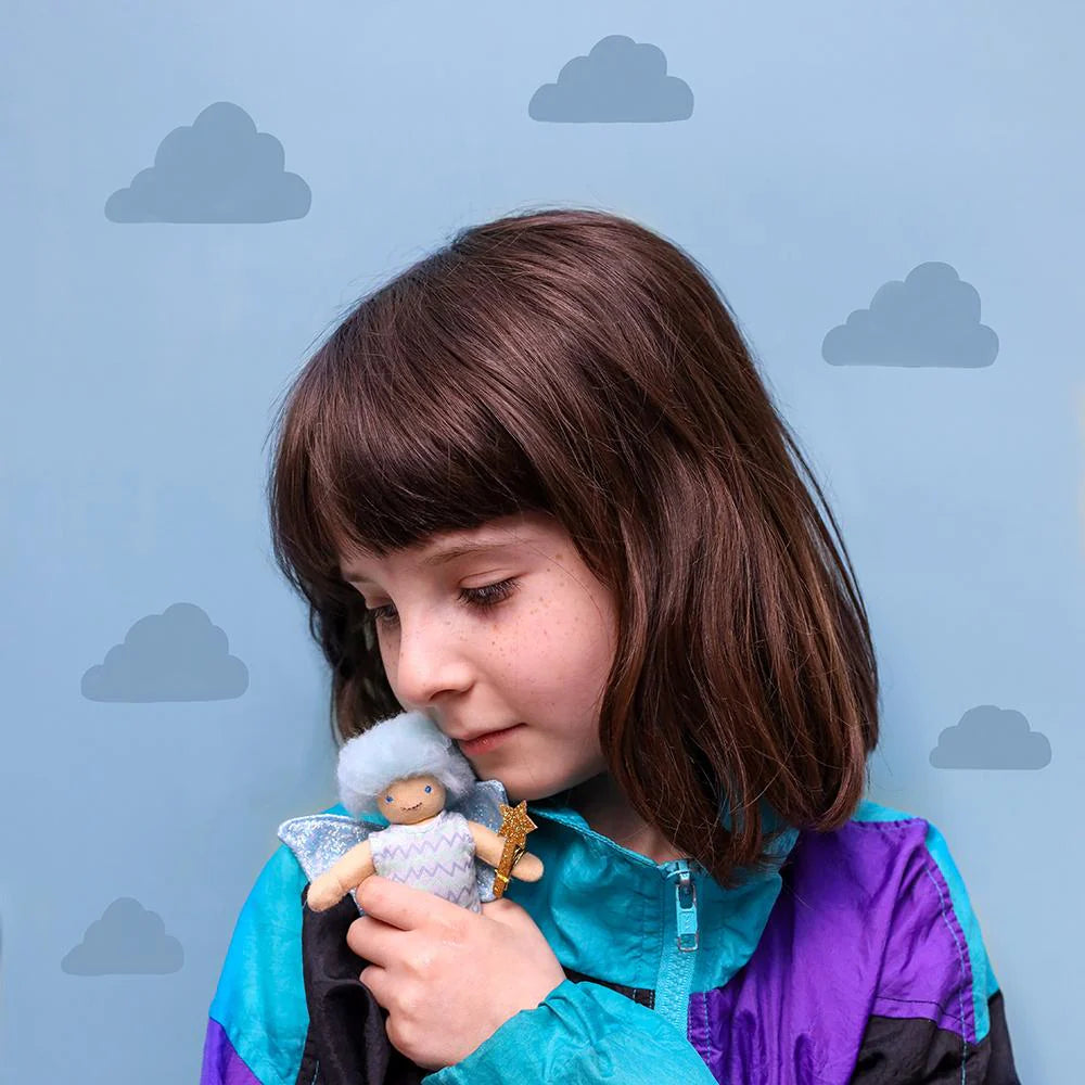Child holding a doll against a blue background with cloud patterns