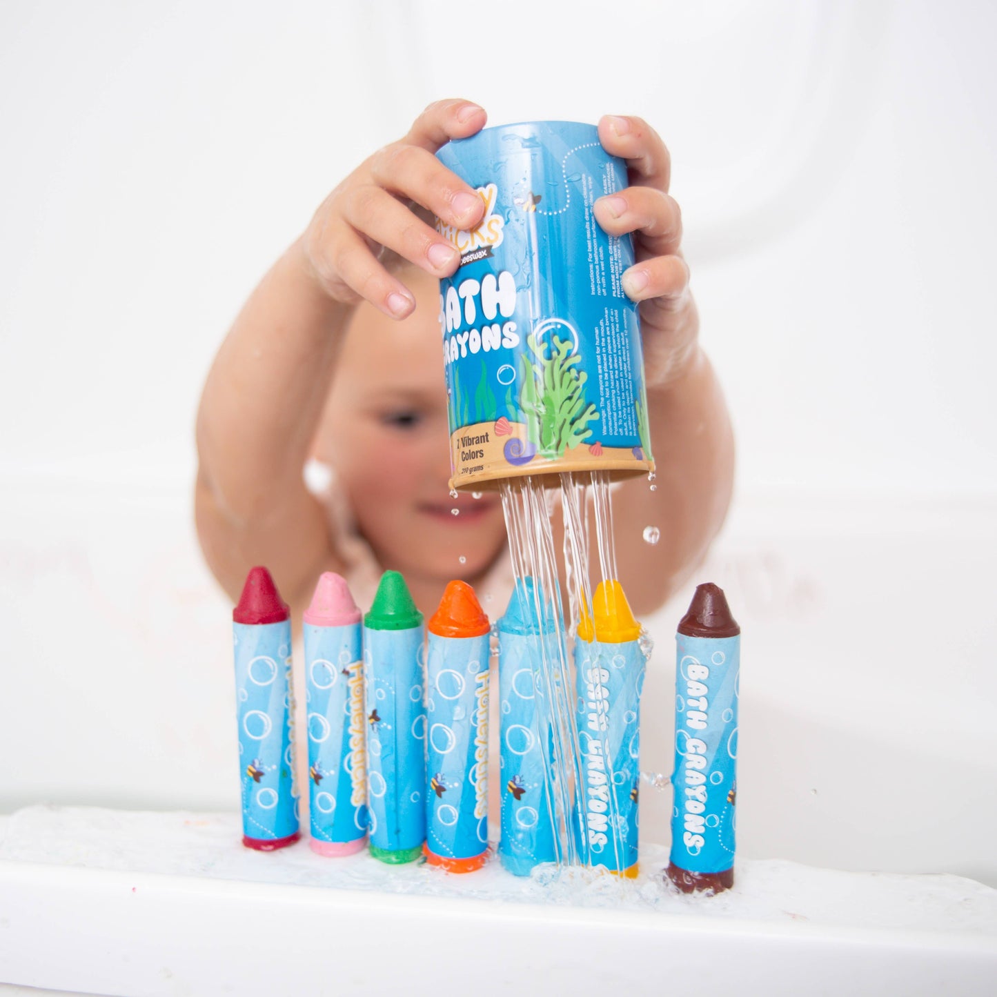 Child's hand pouring colorful bath crayons into a bathtub.