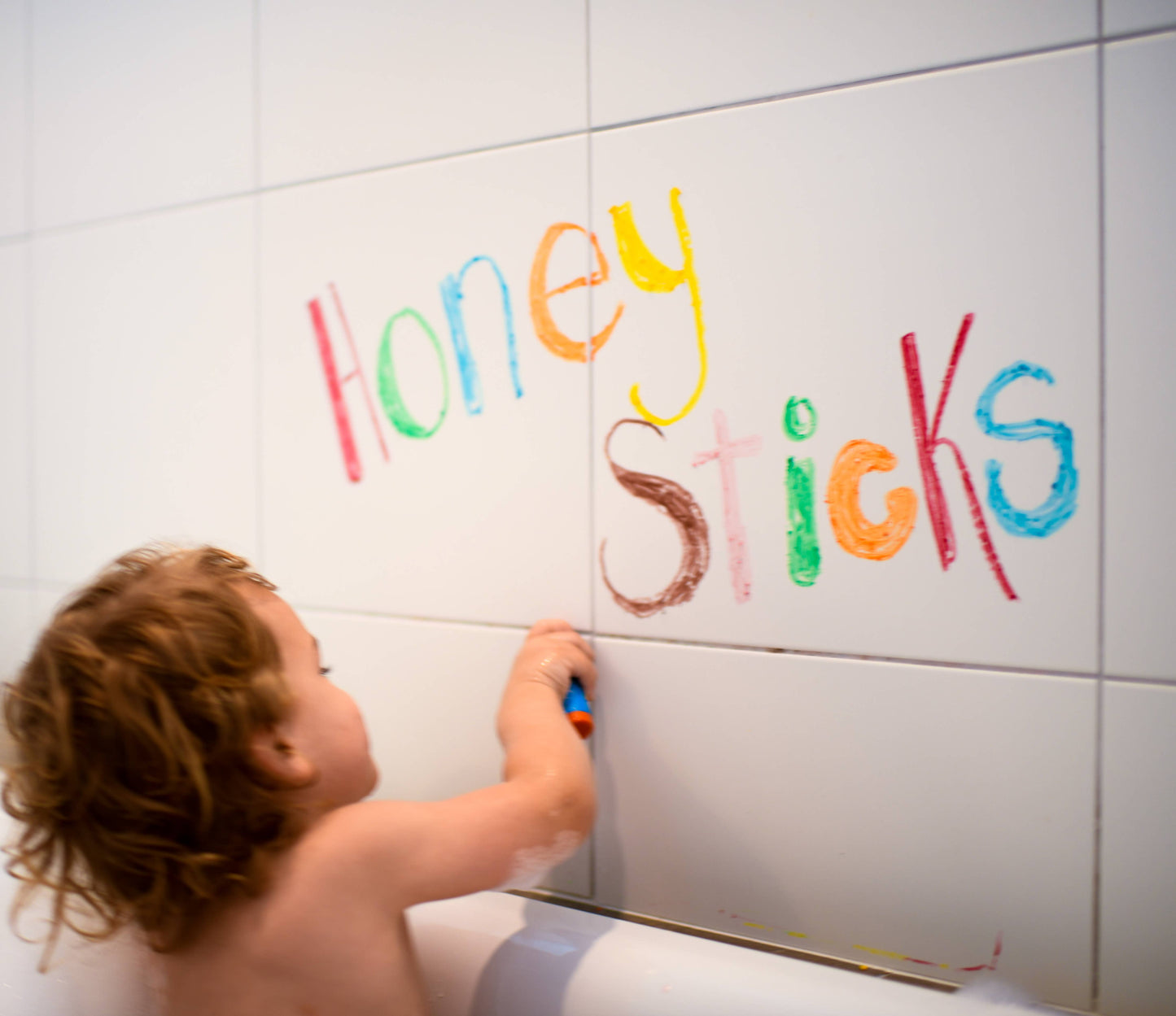 Child writing colorful letters on a tiled wall