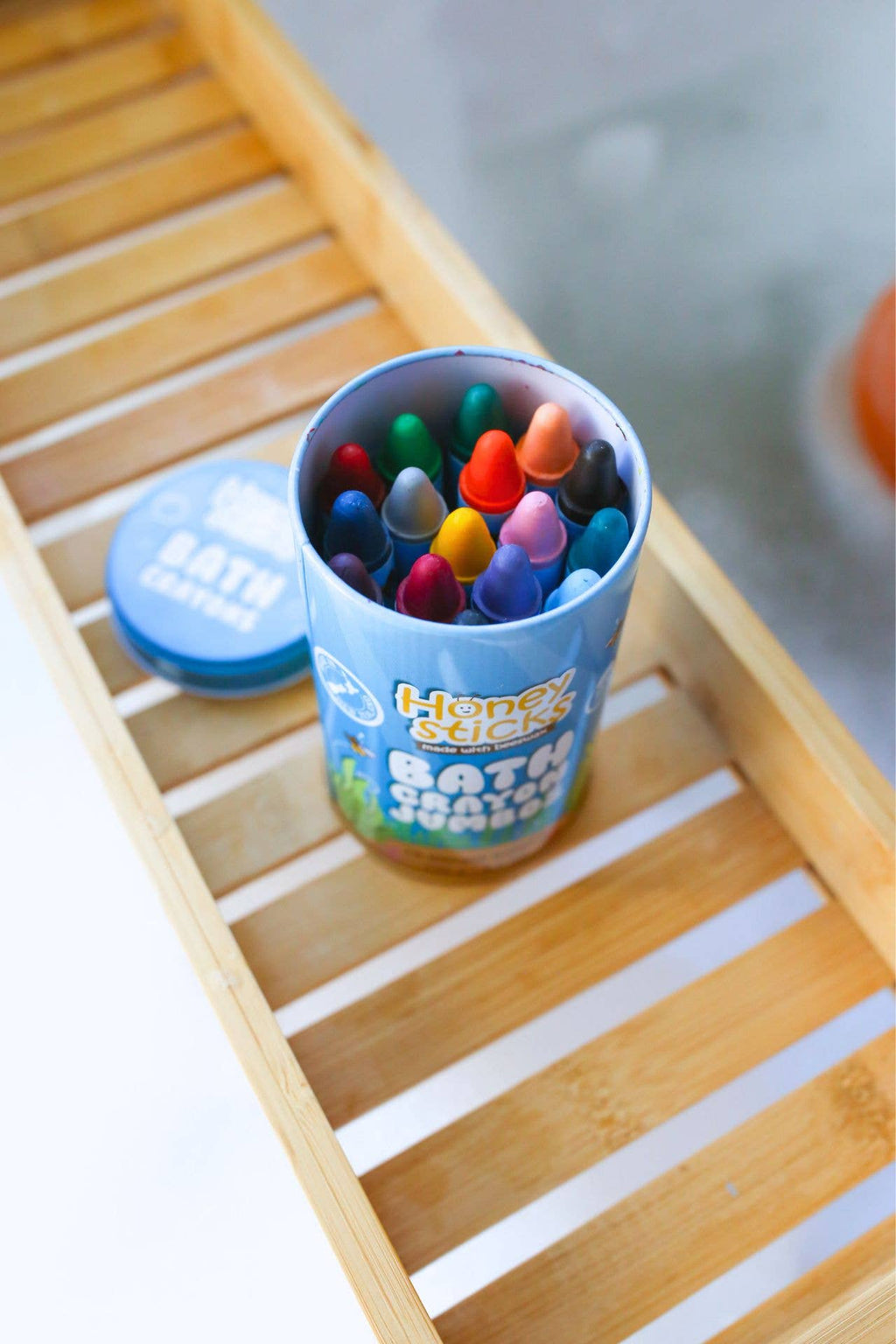 Container of colorful bath crayons on a wooden surface.