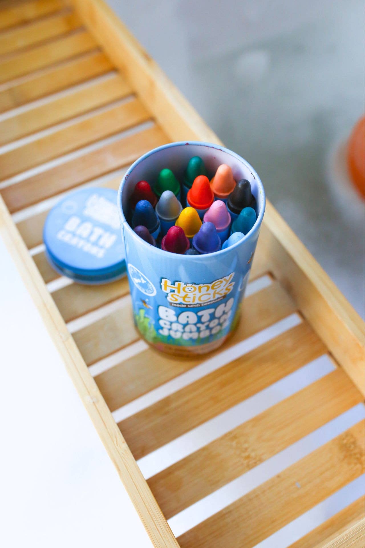 Container of colorful bath crayons on a wooden surface.