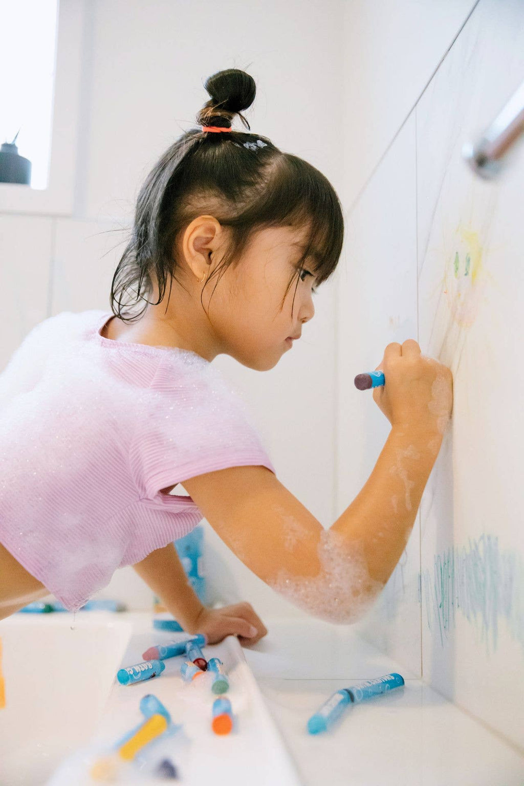 Child drawing on a bath wall with a crayon.