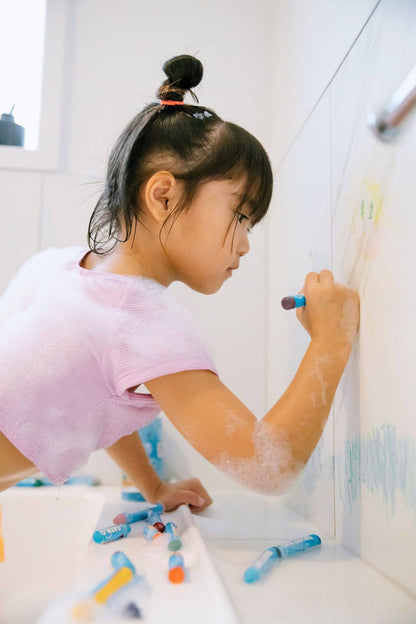Child drawing on a bath wall with a crayon.
