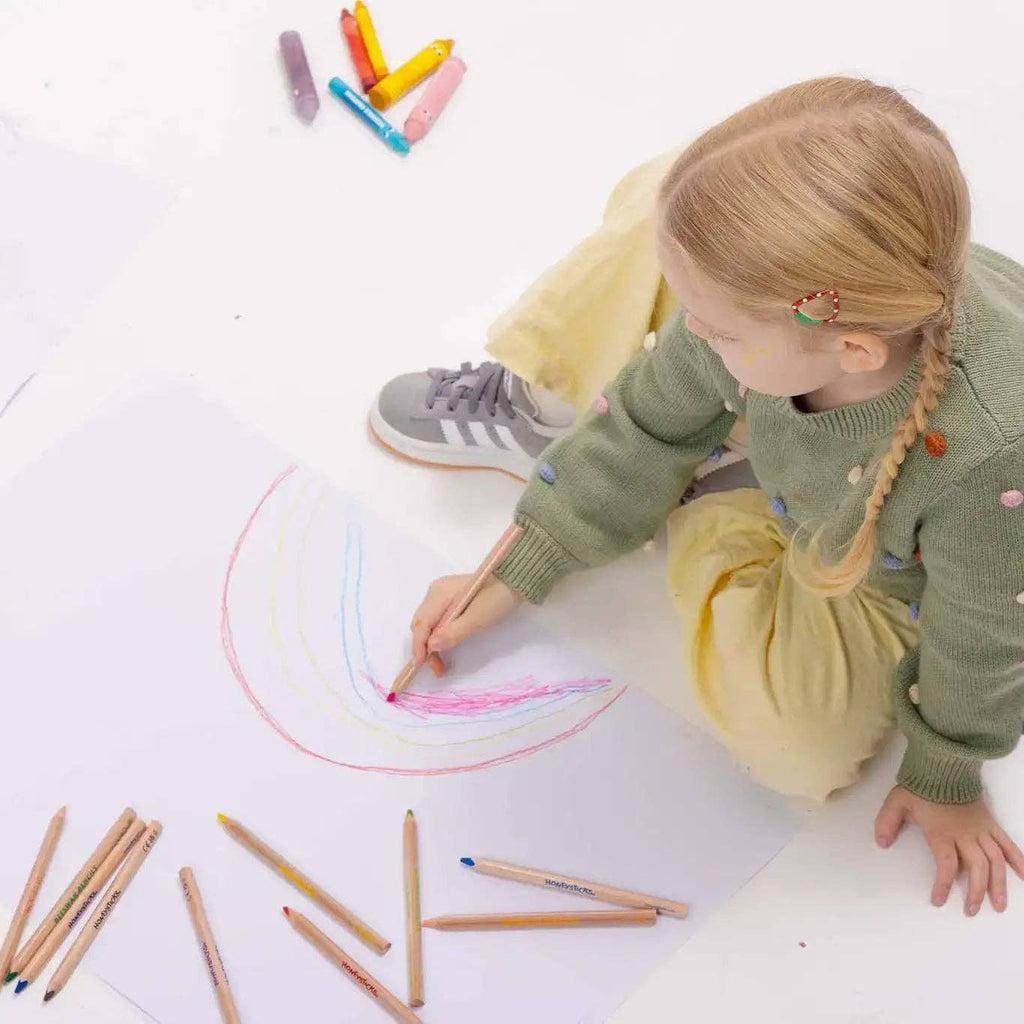 Child drawing a rainbow with colored pencils on a white surface
