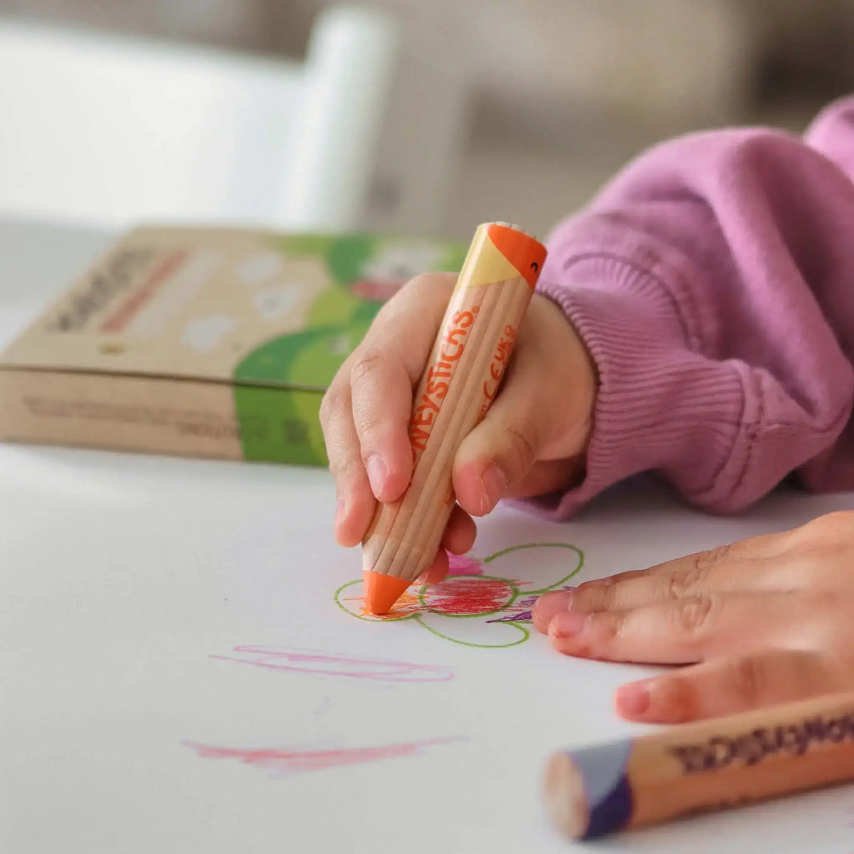 Child's hand holding a crayon over a coloring book with a blurred background