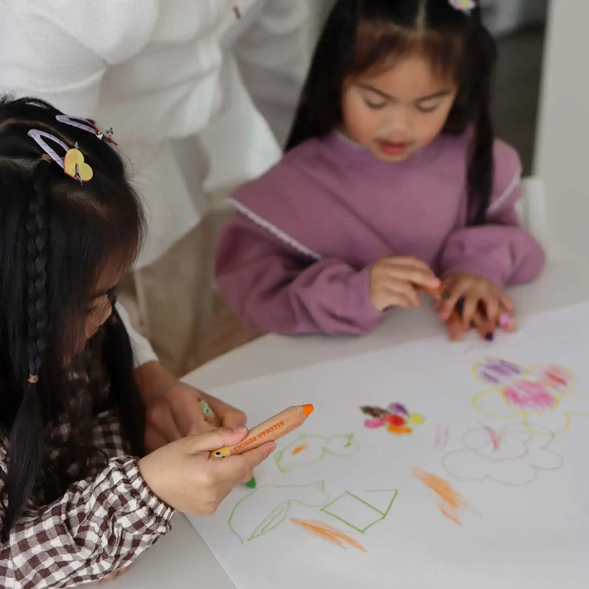 Two children coloring on a large sheet of paper with markers.
