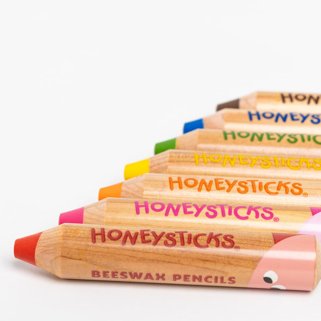 Row of Honeysticks beeswax pencils with colorful tips on a white background