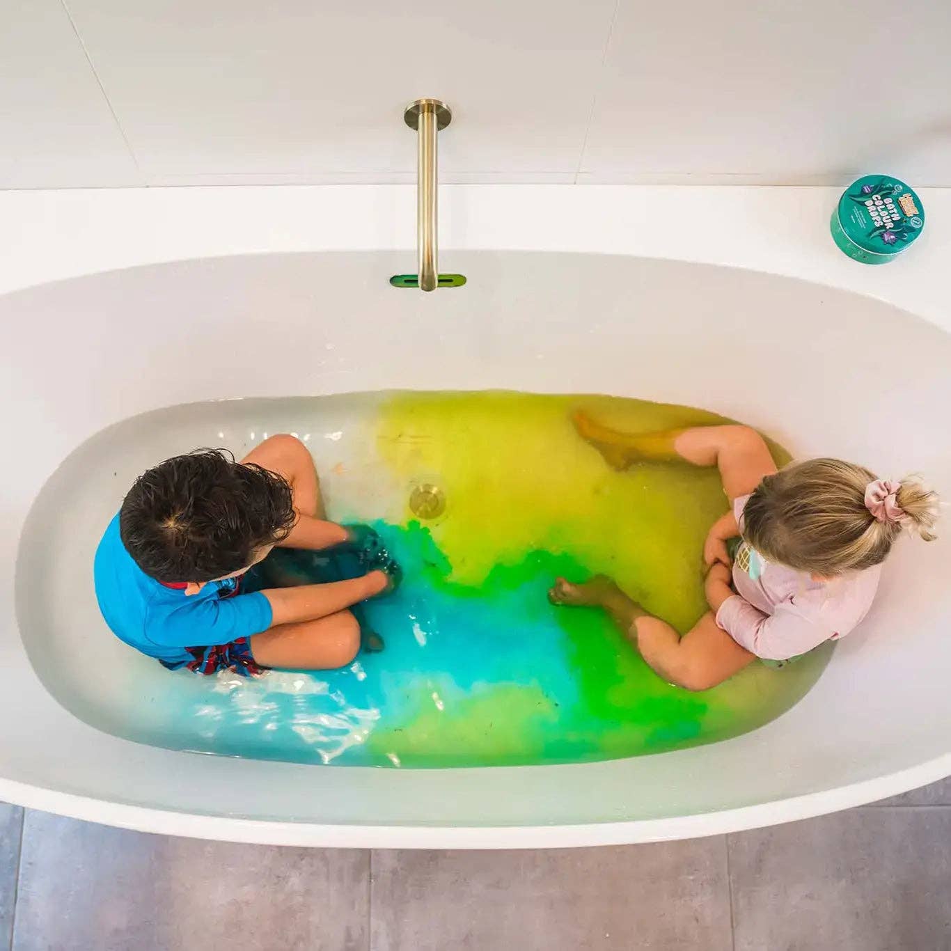 Two children in a bathtub filled with green water, viewed from above.