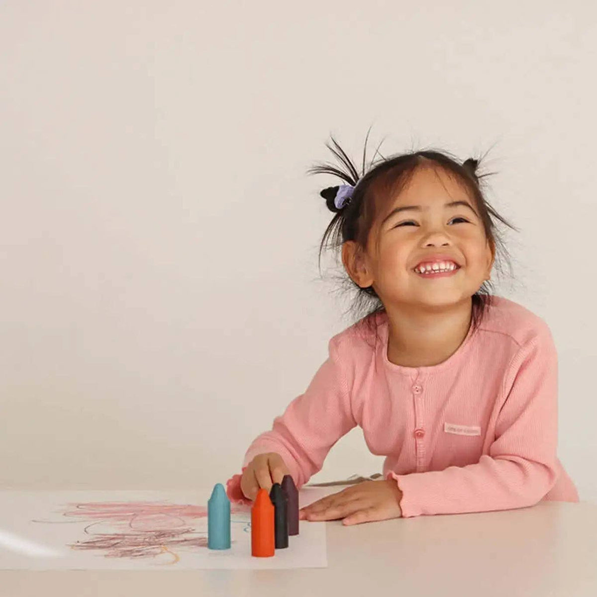 Child in a pink shirt with colorful crayons and a drawing on a light background