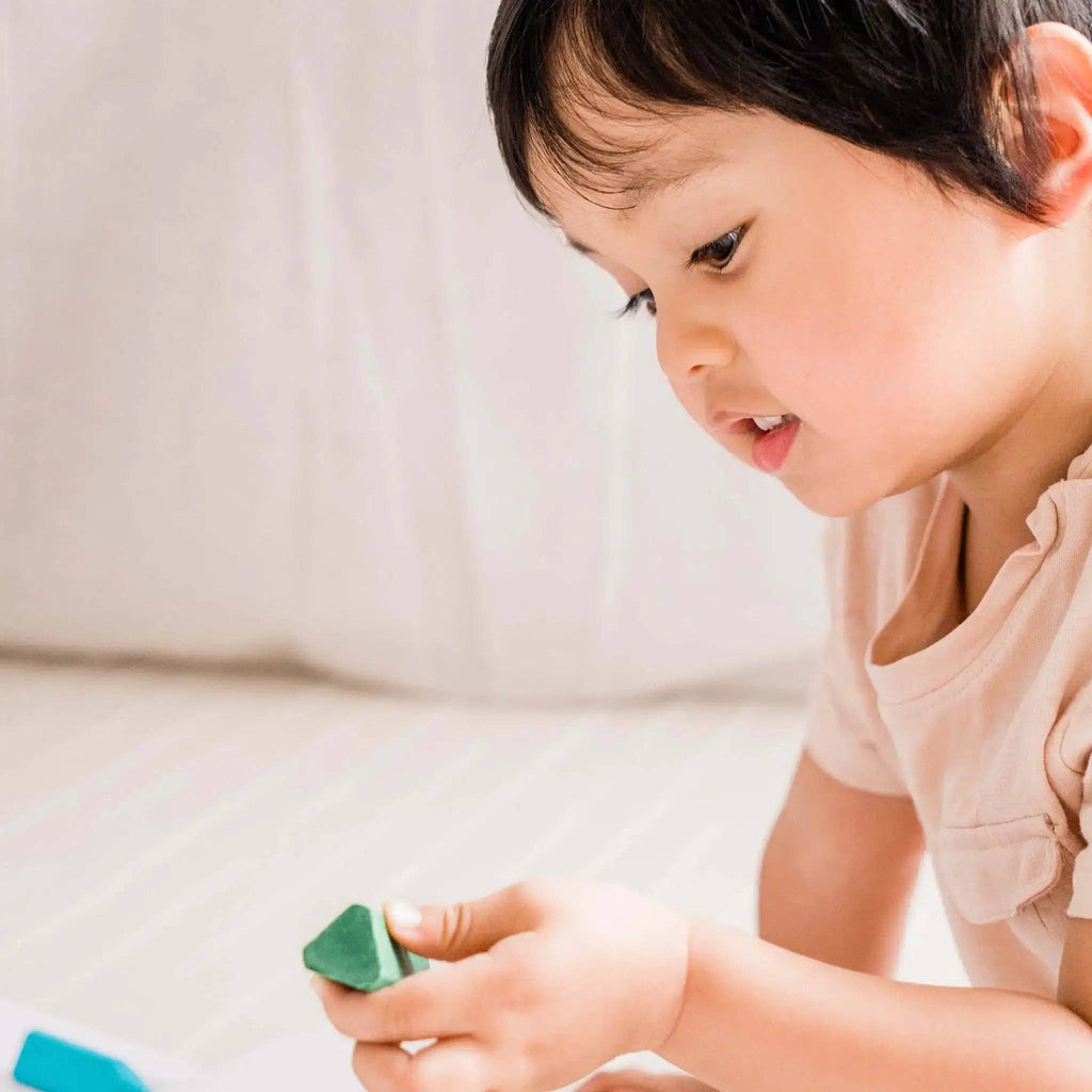 Child holding a green object with a neutral background
