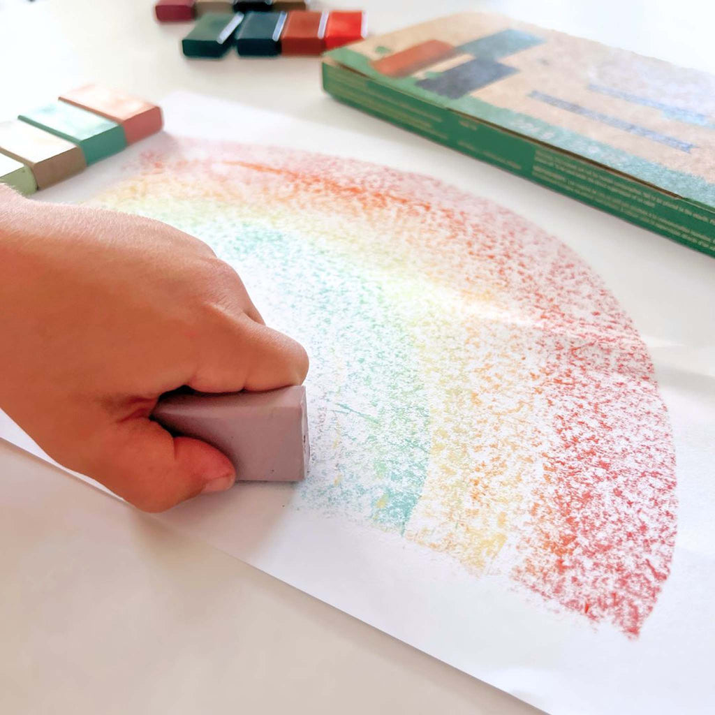 Hand using a crayon to create a rainbow pattern on paper.