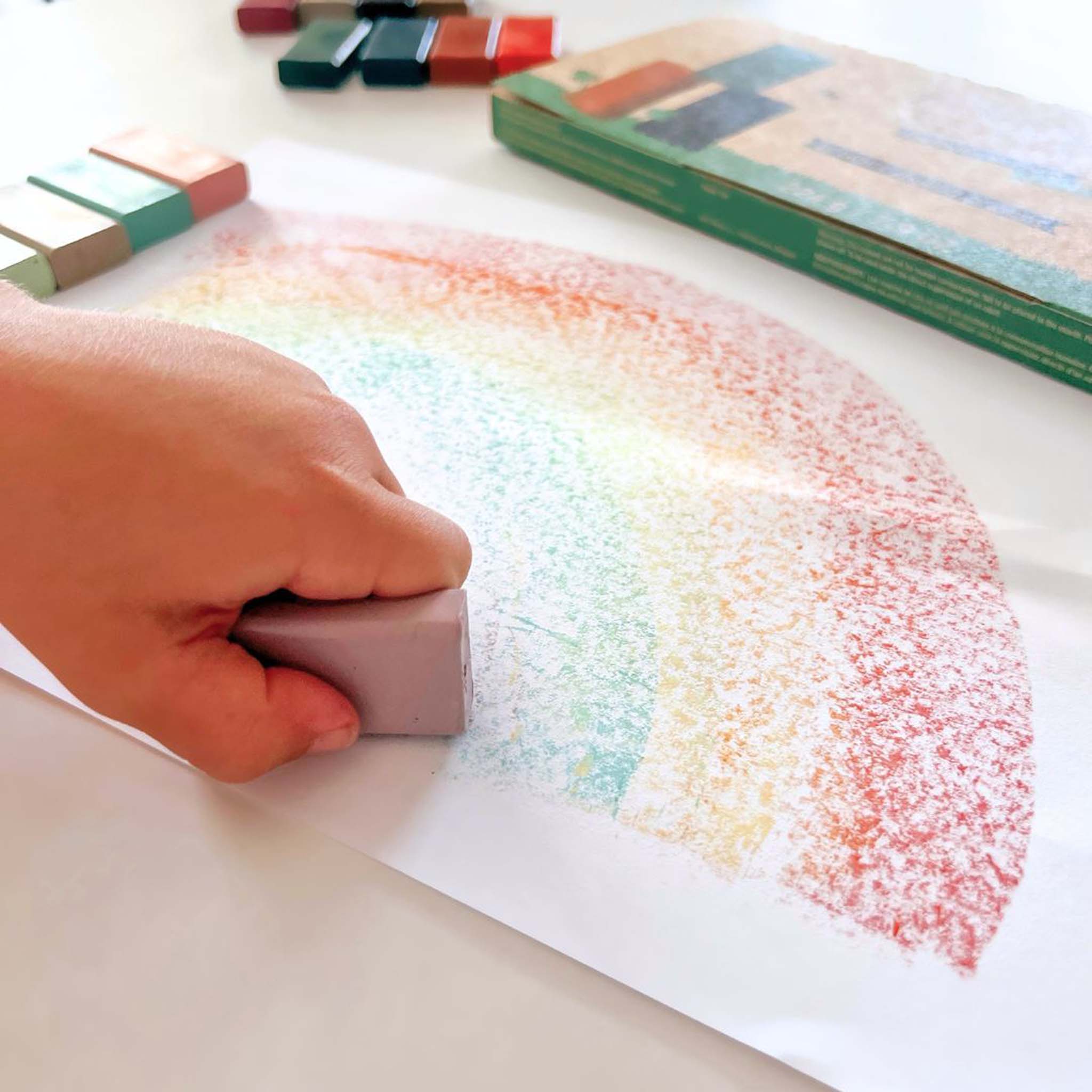 Hand using a crayon to create a rainbow pattern on paper.