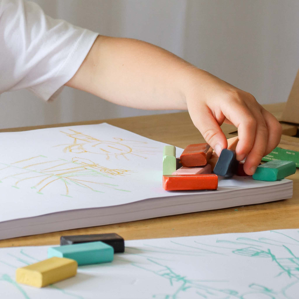 Child's hand playing with colorful crayons on a piece of paper with drawings.