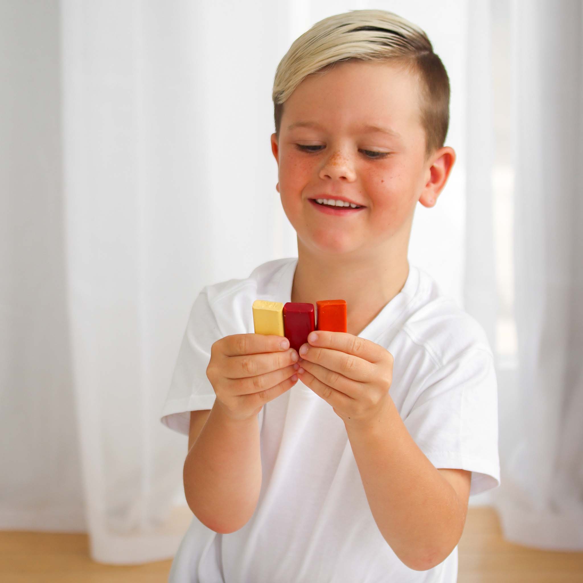 Child holding colorful crayons against a white curtain background