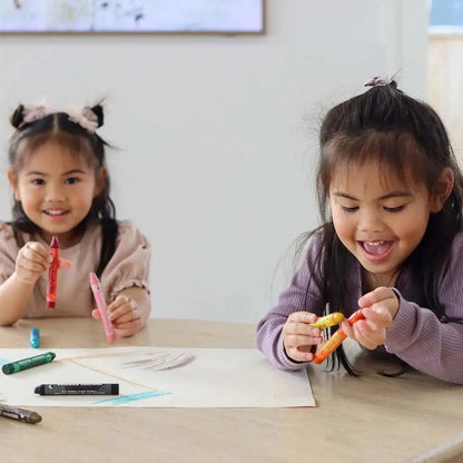 Two young girls sitting at a table with crayons and markers, smiling.