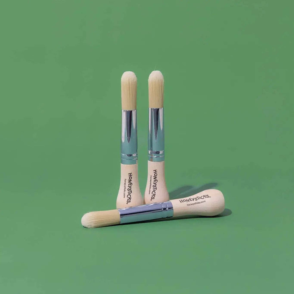 Three wooden makeup brushes with visible branding on a green background