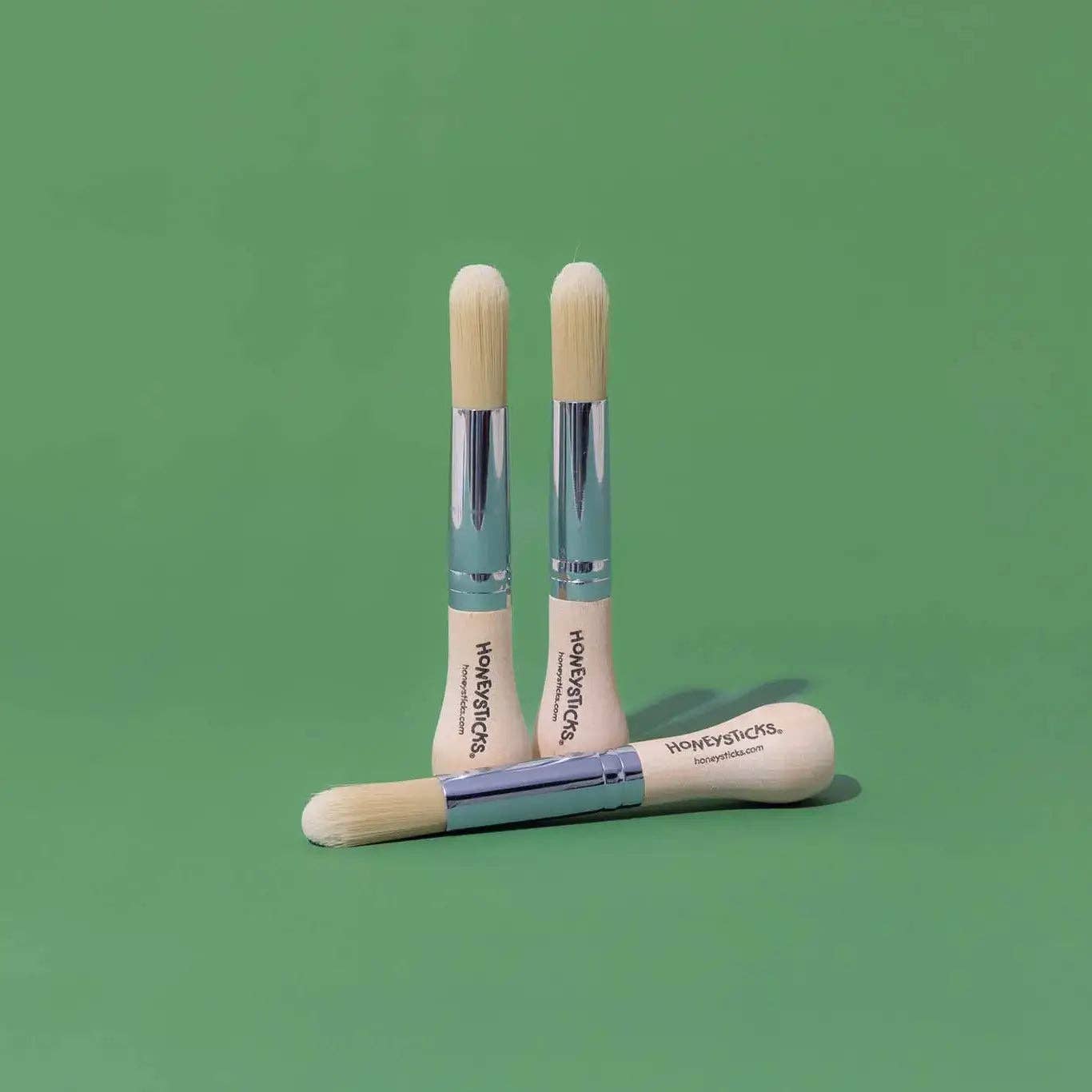 Three wooden makeup brushes with visible branding on a green background