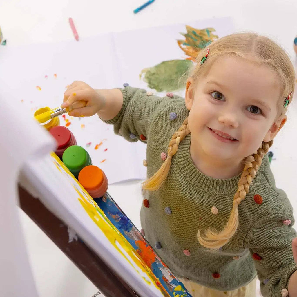 Child painting with a brush and colorful paint on a whiteboard