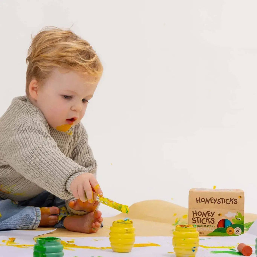 Child playing with colorful honey sticks on a white surface