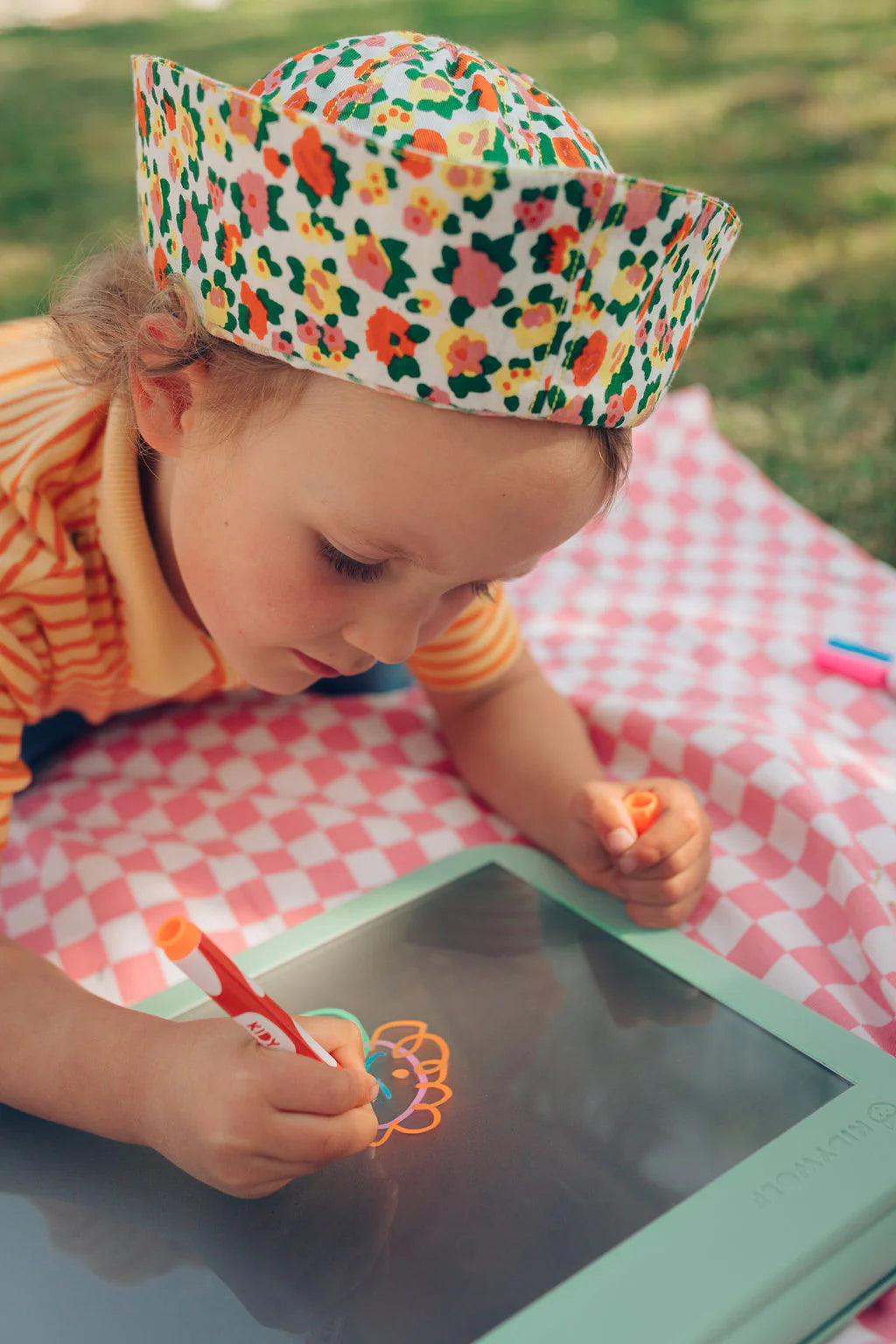 Child drawing on a digital tablet with a colorful hat and checkered blanket
