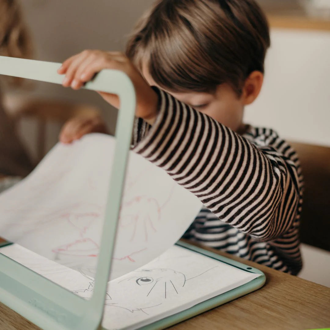 Child in a striped shirt looking at a tablet with drawings on a wooden table