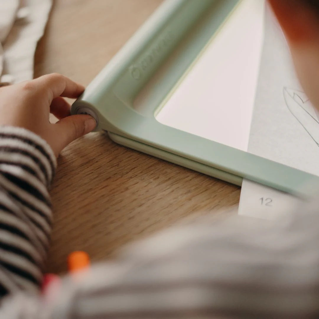Person holding a light green frame over a book on a wooden surface